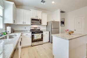 A modern kitchen with white cabinets, stainless steel appliances, a granite countertop, and a small island.