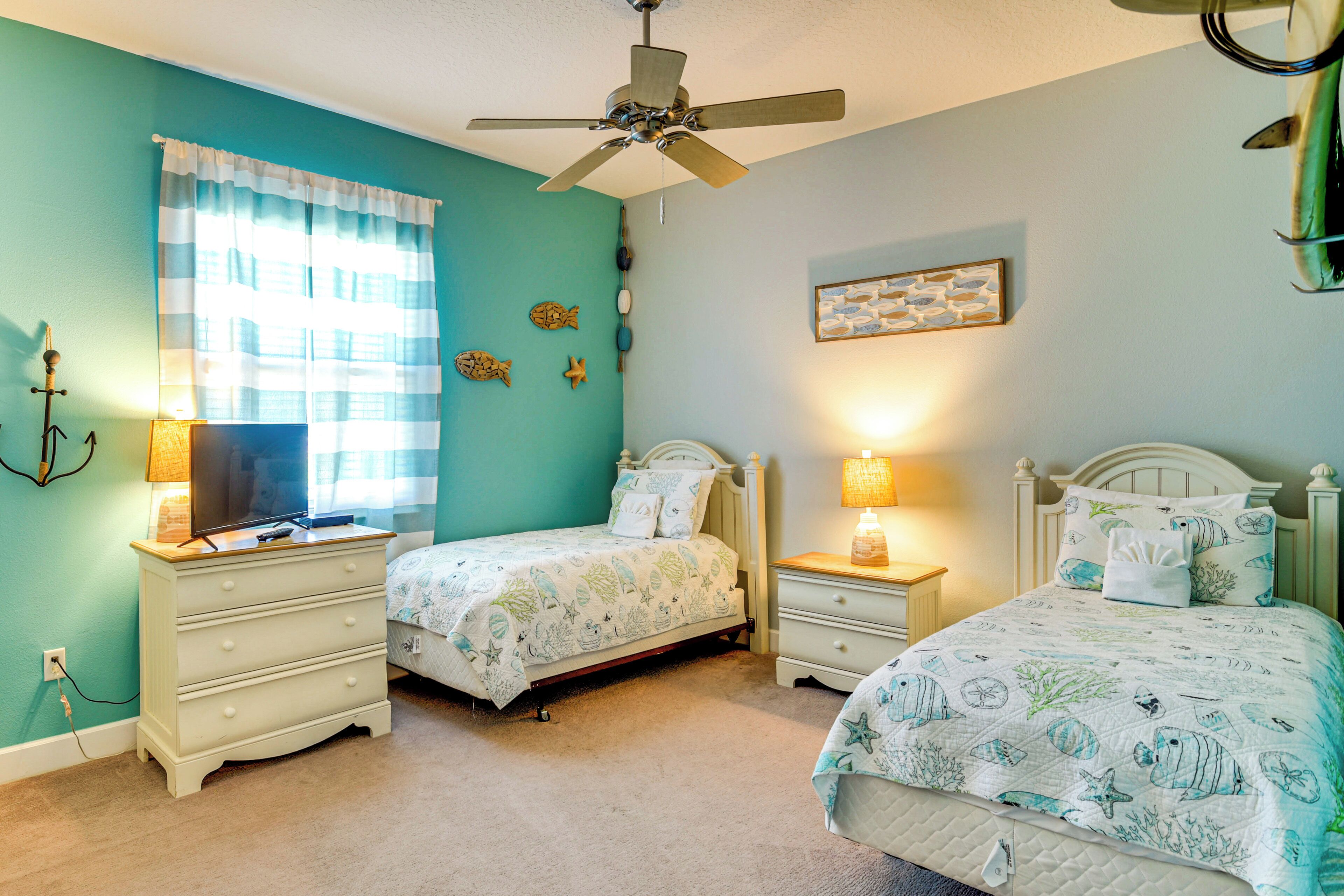 A bedroom with two beds, a ceiling fan, and a window with curtains.