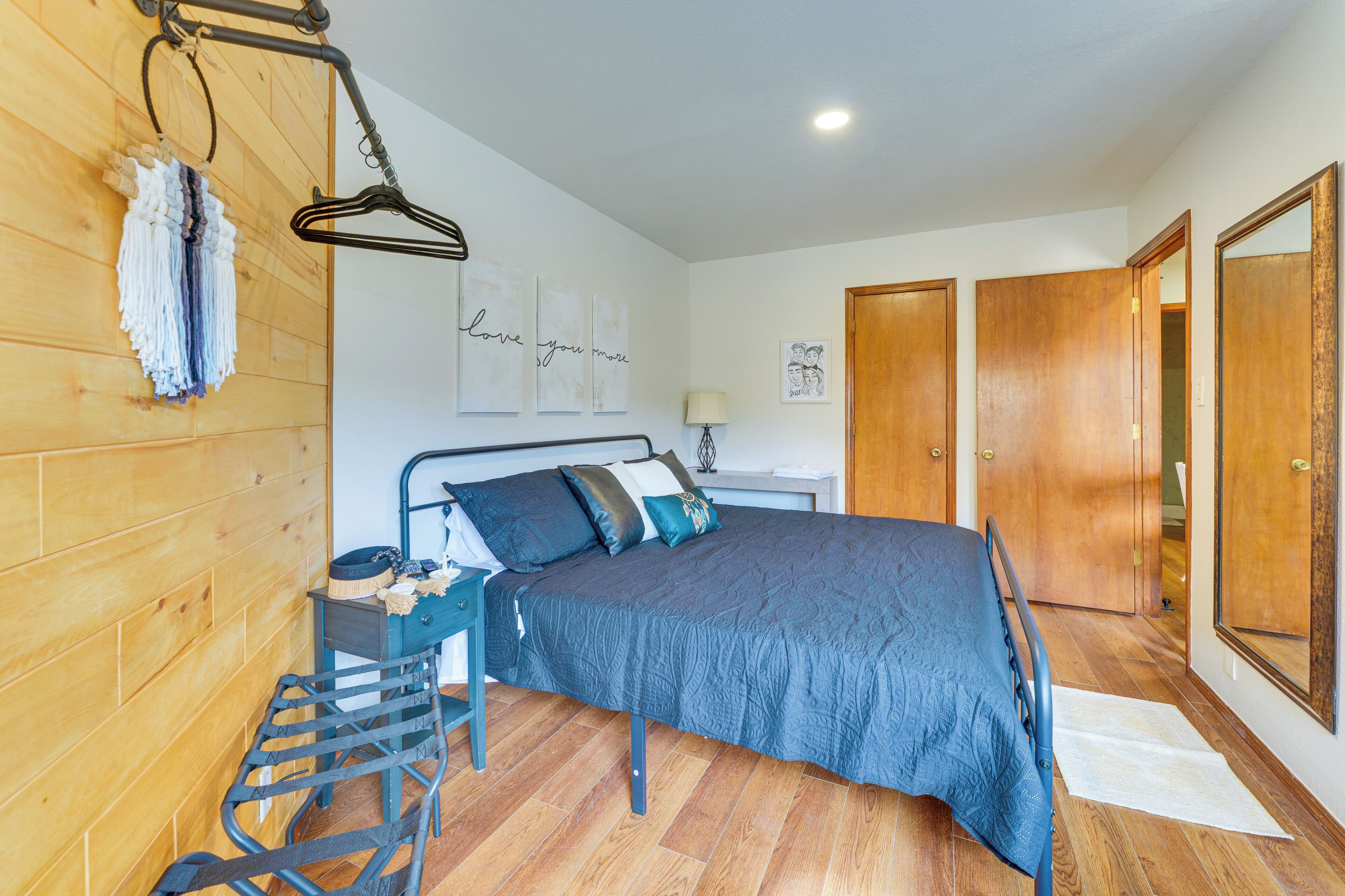 A bedroom with a bed, a nightstand, a chair, wooden walls, a door, and artwork on the wall.