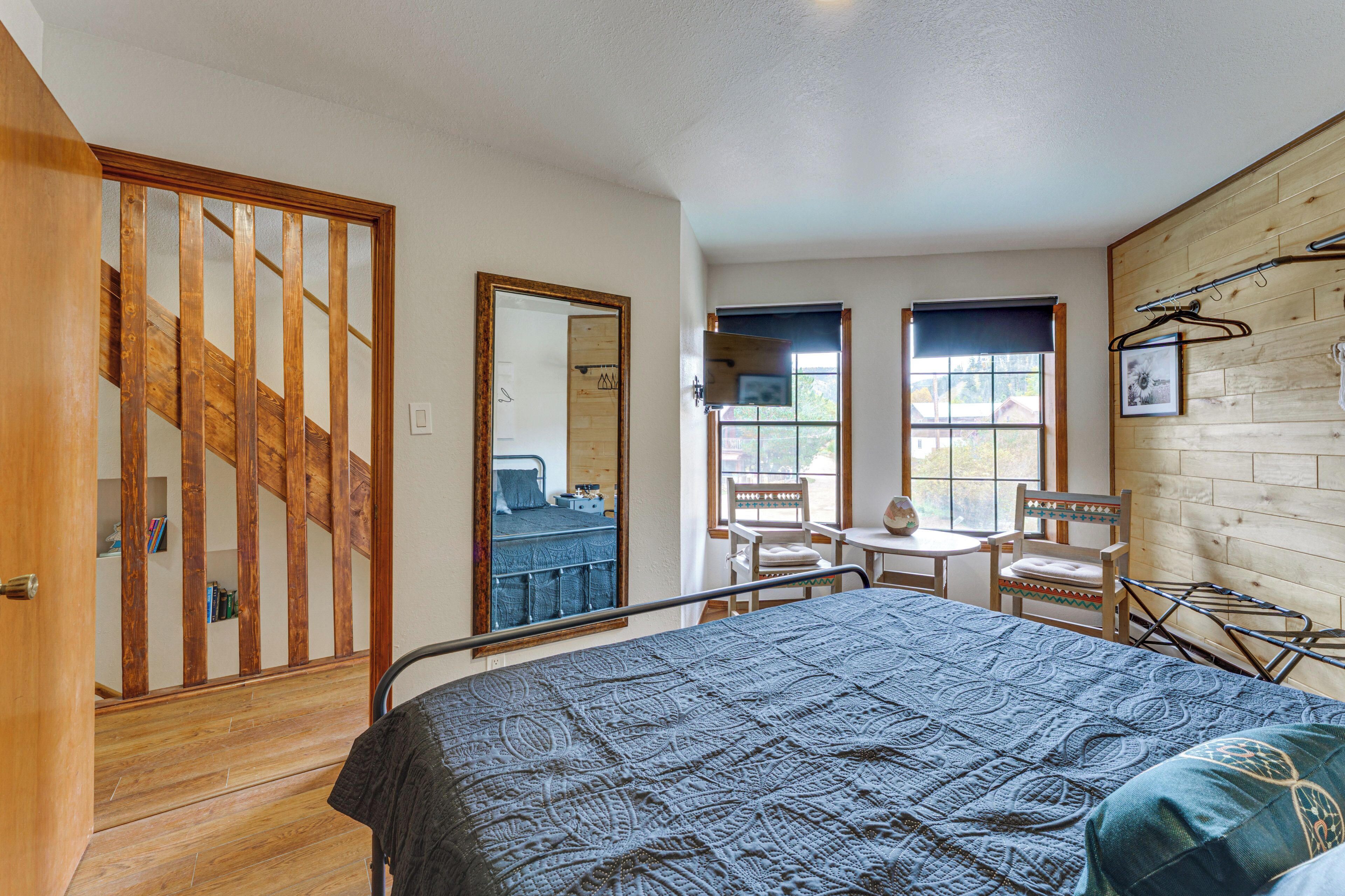 A bedroom with a bed, a wooden staircase, a small table, two chairs, and a window with a view.