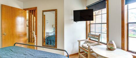 Un dormitorio con una cama, una silla, una mesa, un televisor y una ventana.