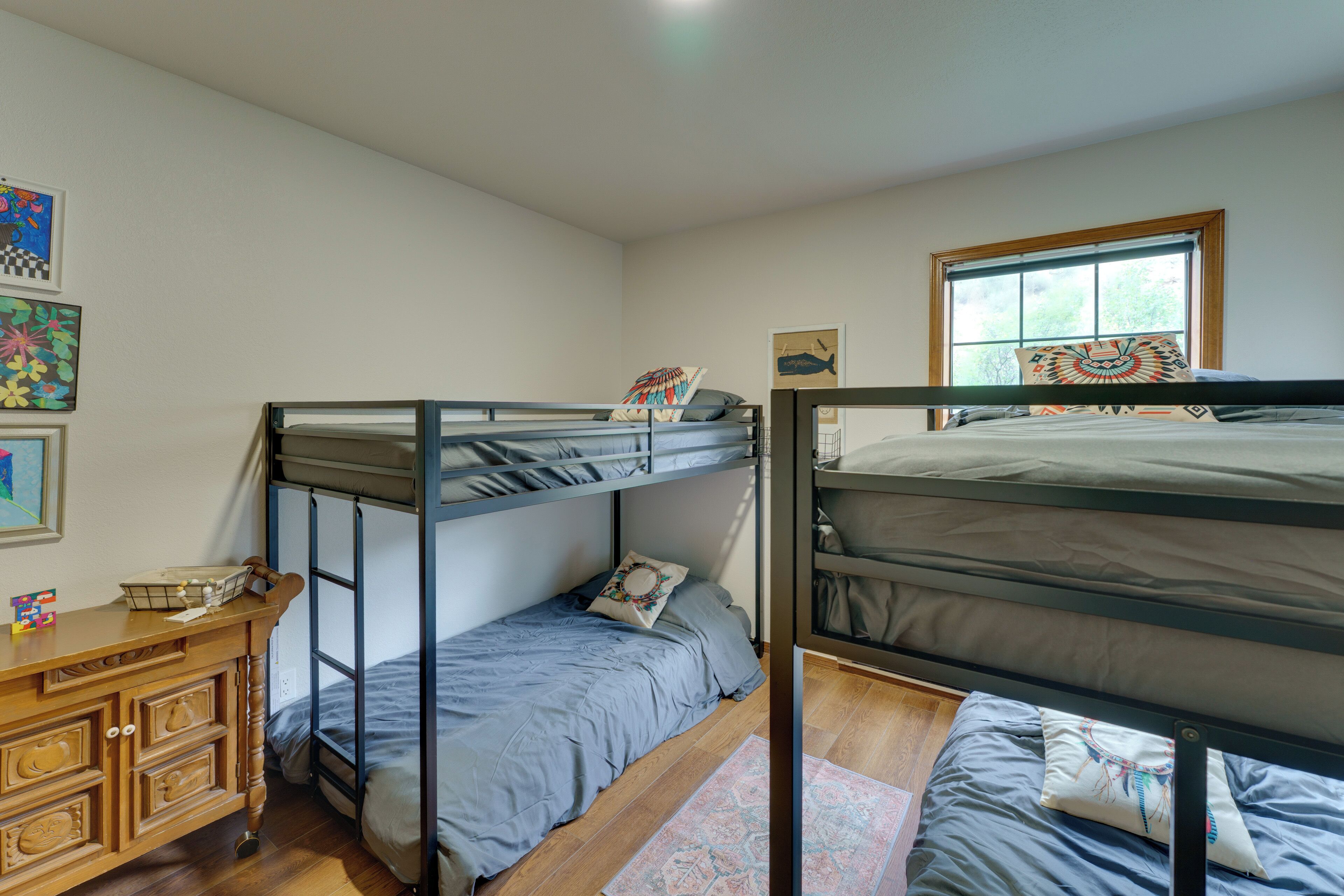 A bunk bed room with a wooden dresser, a window with a view, and artwork on the walls.