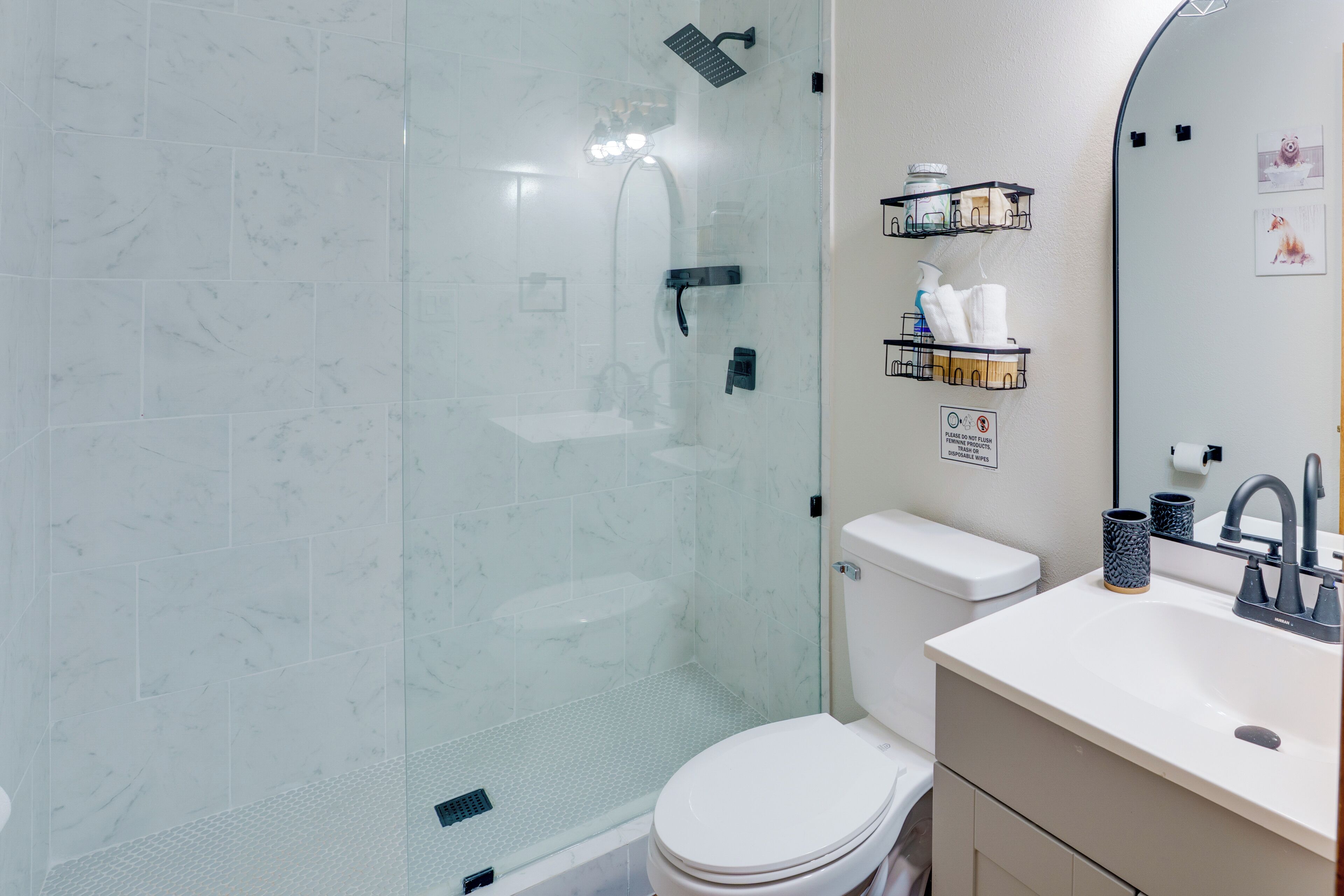 A modern bathroom with a glass-enclosed shower, a white toilet, and a sink with a mirror.