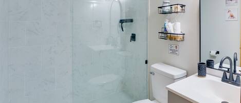 A modern bathroom with a glass-enclosed shower, a white toilet, and a sink with a mirror.