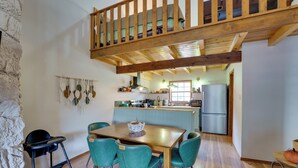 Un coin repas avec une table en bois et quatre chaises, un plafond en bois haut et une cuisine à l’arrière-plan.