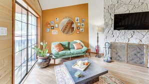 Un salon chaleureux avec un canapé vert, une table basse et un mur en pierre sur lequel est fixé un téléviseur.