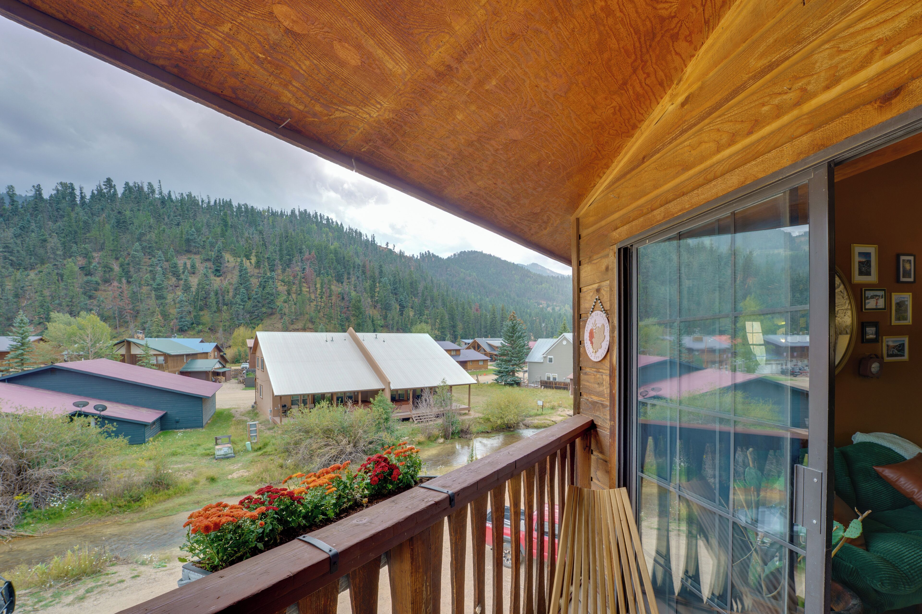 Een houten balkon met uitzicht op een bebost gebergte en enkele gebouwen.