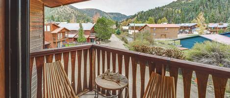 A wooden balcony with two wooden chairs and a small round table.