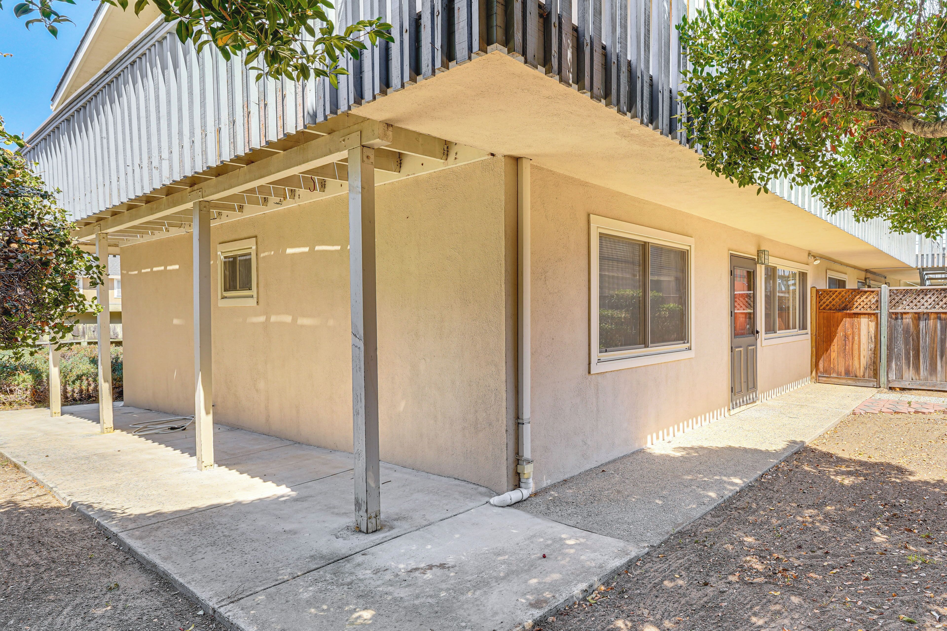 A covered patio area with a concrete floor, metal columns, and a beige wall.