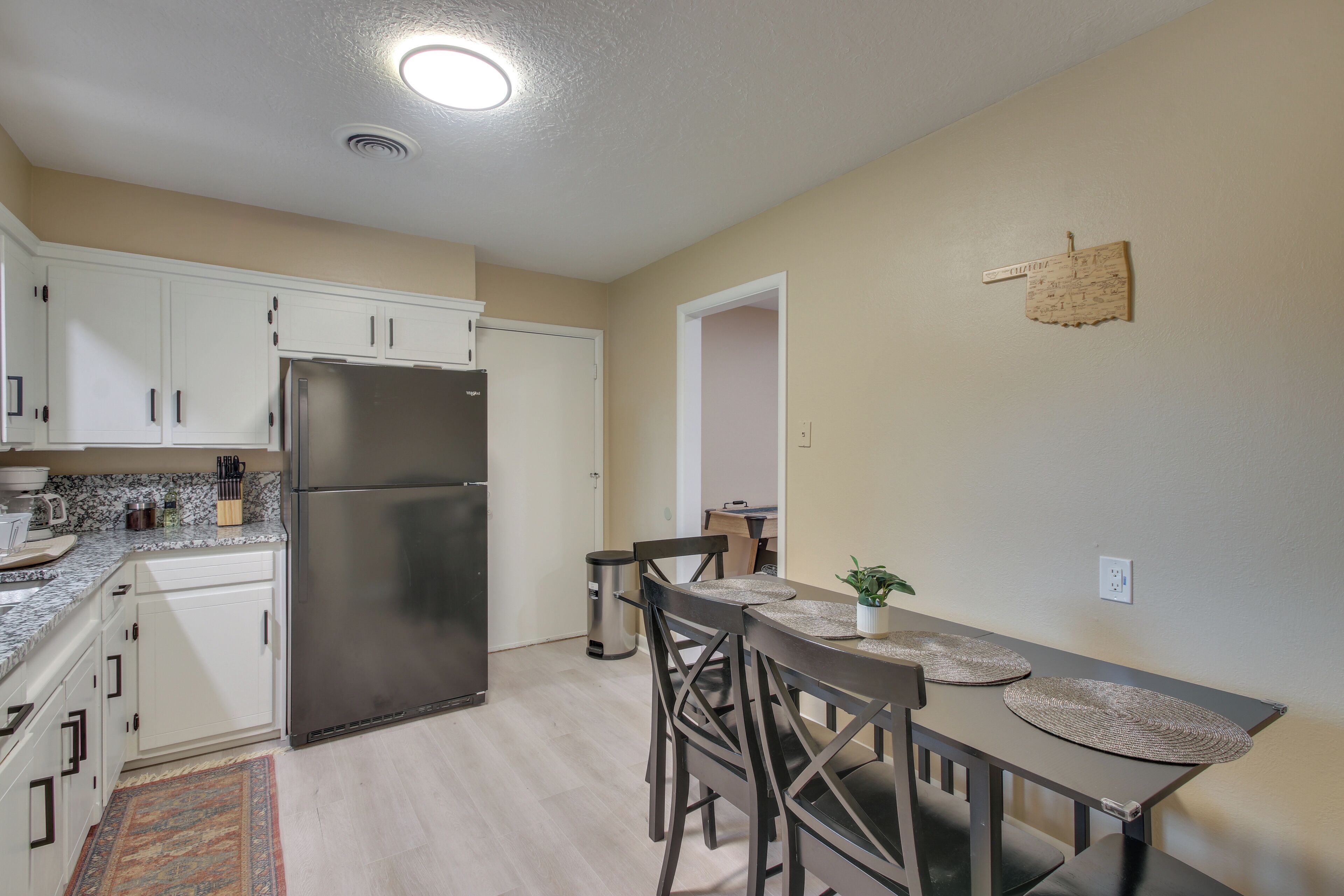 Una cocina con armarios blancos, un refrigerador de acero inoxidable y una mesa de comedor con sillas.