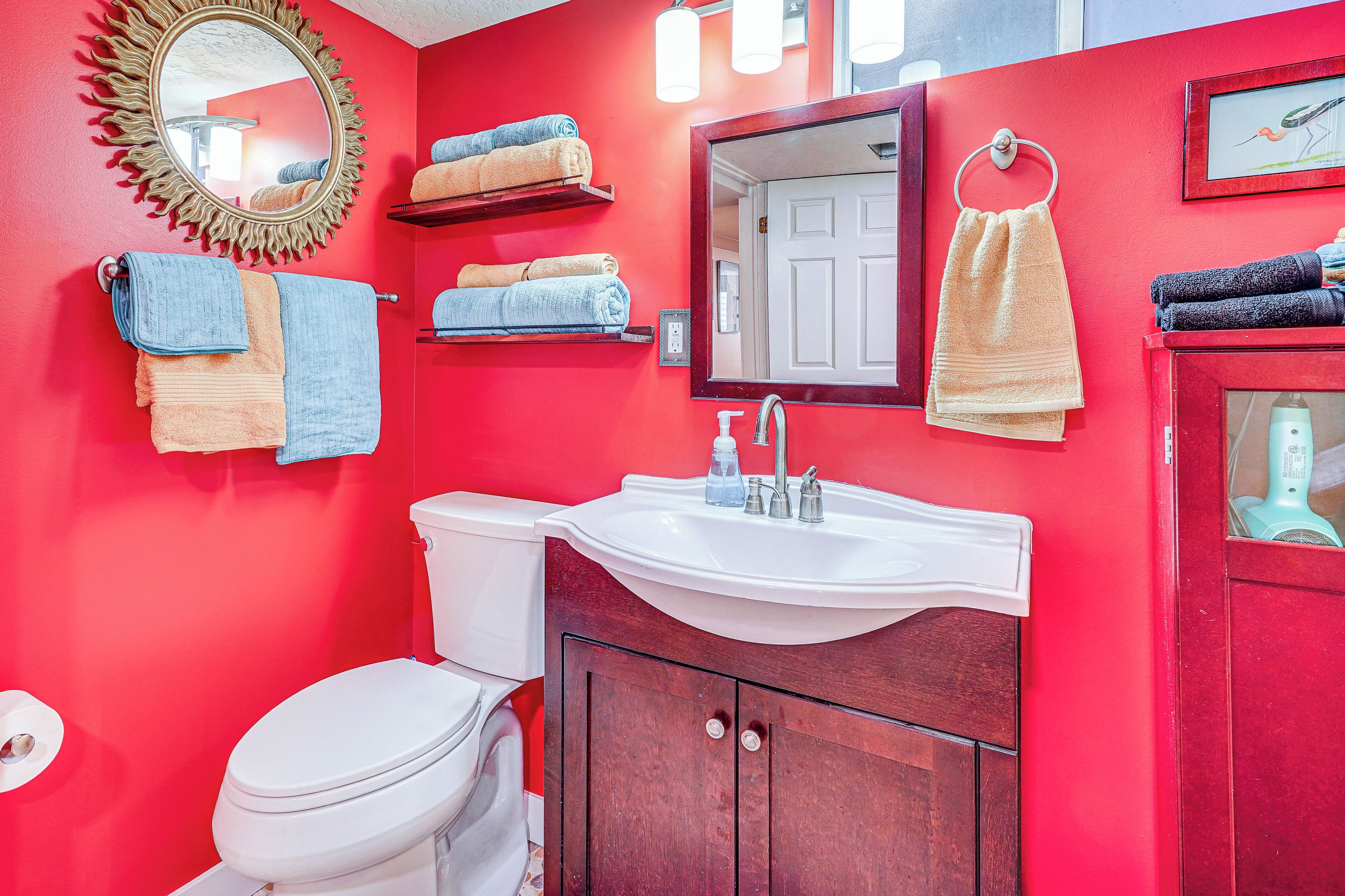 Ein Badezimmer mit roter Wand, Waschbecken in Weiß, einem Spiegel und mehreren Handtüchern.