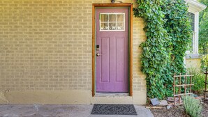 Eine violette Tür mit kleinem Fenster, eine Ziegelwand und ein grüner Efeu, der über die Wand wächst.