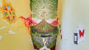 Ein farbenfrohes Wandgemälde mit Baum, Wasserfall und Schmetterlingen.