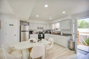 A modern kitchen with white cabinetry, a dining table with four chairs, and a stainless steel refrigerator.