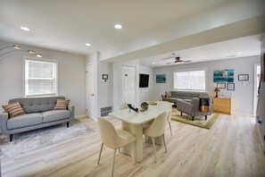 Een ruime woonkamer met een grijze bank, beige fauteuils, een witte eettafel en een grijze fauteuil.