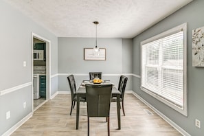 A dining area with a table, chairs, a hanging light fixture, and a window with blinds.