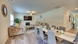 A modern living room with a sofa, dining table, and chairs, a fireplace, and a ceiling fan. - Walk to Beach: Group Getaway in Coastal Virginia (Norfolk)