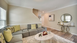 A living room with a gray sectional sofa, a round coffee table, and a staircase leading to another level. - Walk to Beach: Group Getaway in Coastal Virginia (Norfolk)