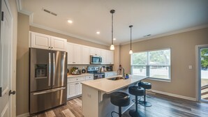 A modern kitchen with white cabinets, stainless steel appliances, and a large island with bar stools. - Walk to Beach: Group Getaway in Coastal Virginia (Norfolk)