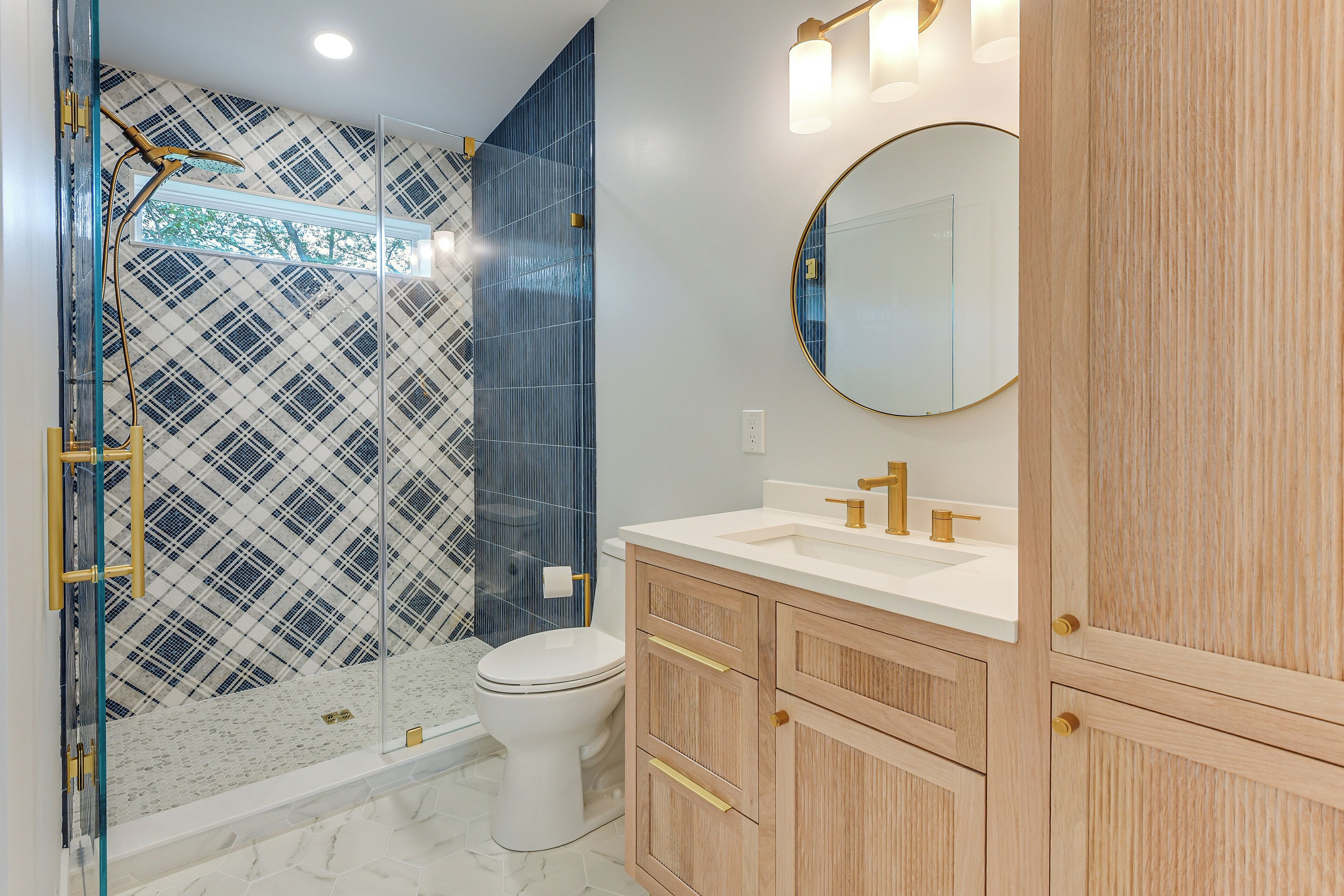 A modern bathroom with a glass-enclosed shower, a white toilet, and a wooden vanity with a round mirror.