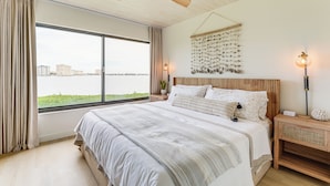 A bedroom with a large bed, a ceiling fan, a view of the city, and a wall art piece.
