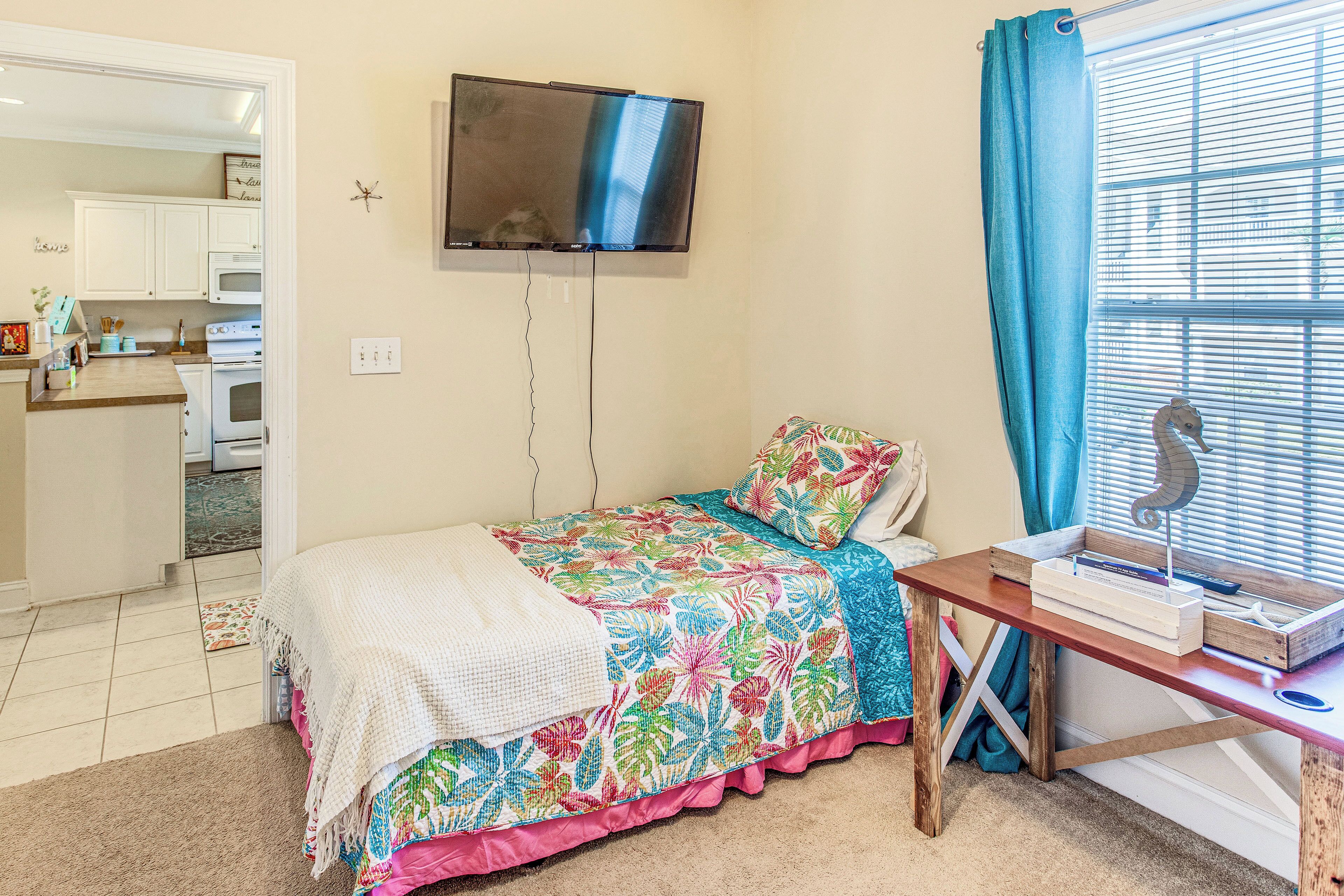 A bedroom with a bed, a desk, a TV, and a window with curtains.