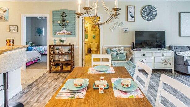 A dining area with a wooden table set for four, a chandelier, and a clock on the wall.