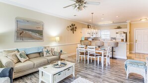 A spacious living room with a beige sofa, a white coffee table, and a dining area with white chairs.
