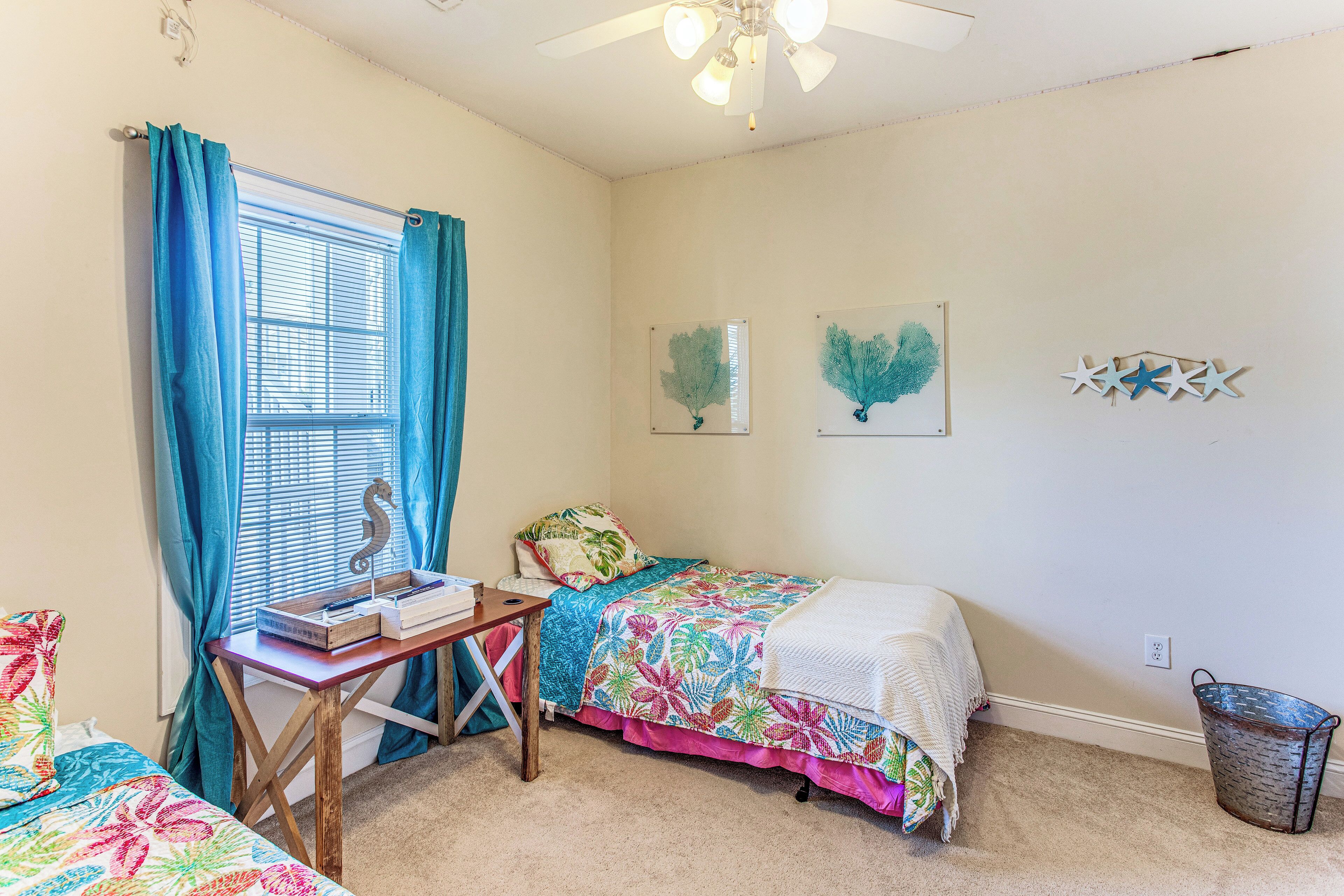 A bedroom with two beds, a desk, a window with curtains, and wall art.