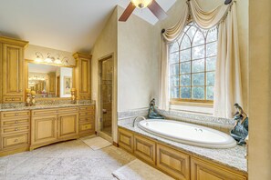 A spacious bathroom with a large bathtub, a vanity with a mirror, and a window with curtains.