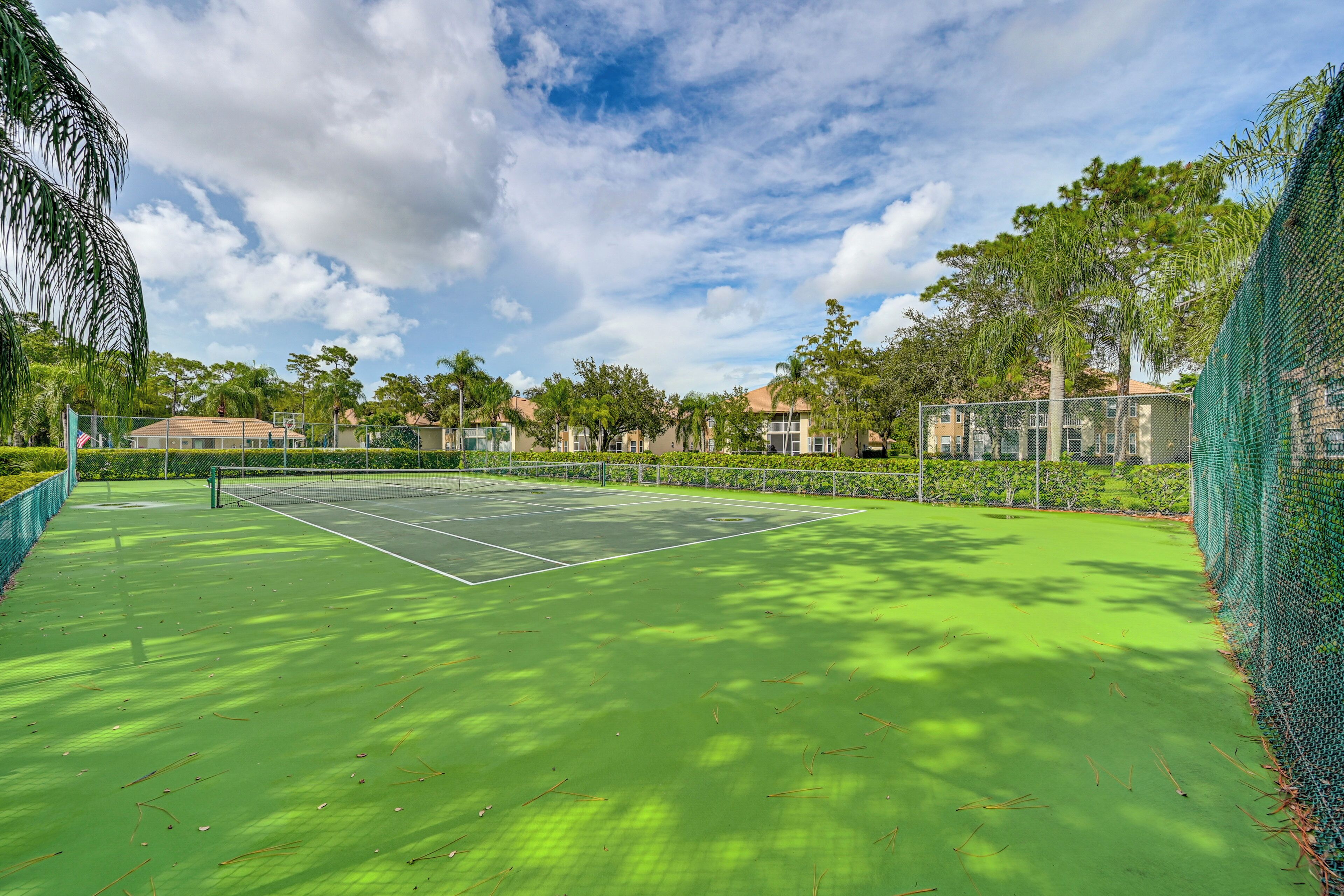 Ein Tennisplatz mit grüner Belag, umgeben von Bäumen und einem Zaun.