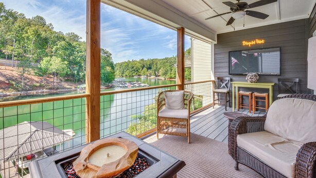 Un balcon donnant sur un lac, des meubles en osier, un ventilateur de plafond et un panneau lumineux au néon.