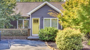 Une maison de plain-pied à l’extérieur gris foncé, avec une porte d’entrée jaune et un petit porche.