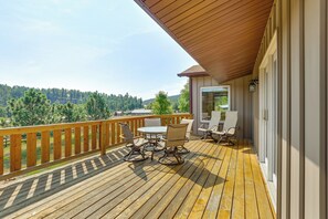 A wooden deck with outdoor furniture, a view of a forest, and a building with a covered area.