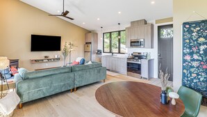 Una sala de estar moderna con un sofá verde, una mesa de comedor de madera y un televisor de pantalla plana montado en la pared.