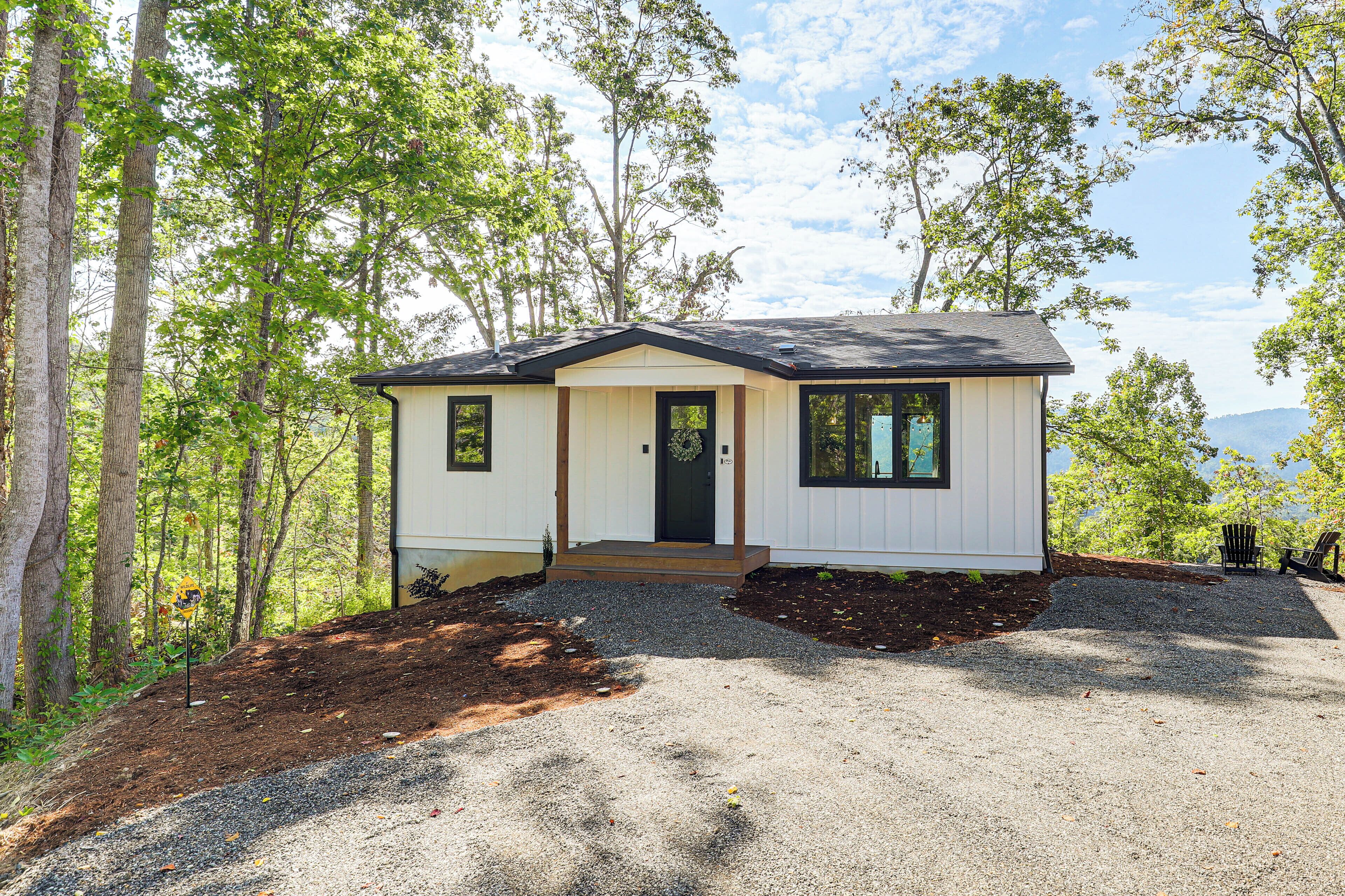 A single-story house with a front porch, a gravel driveway, and a landscape with trees and a mountain view.