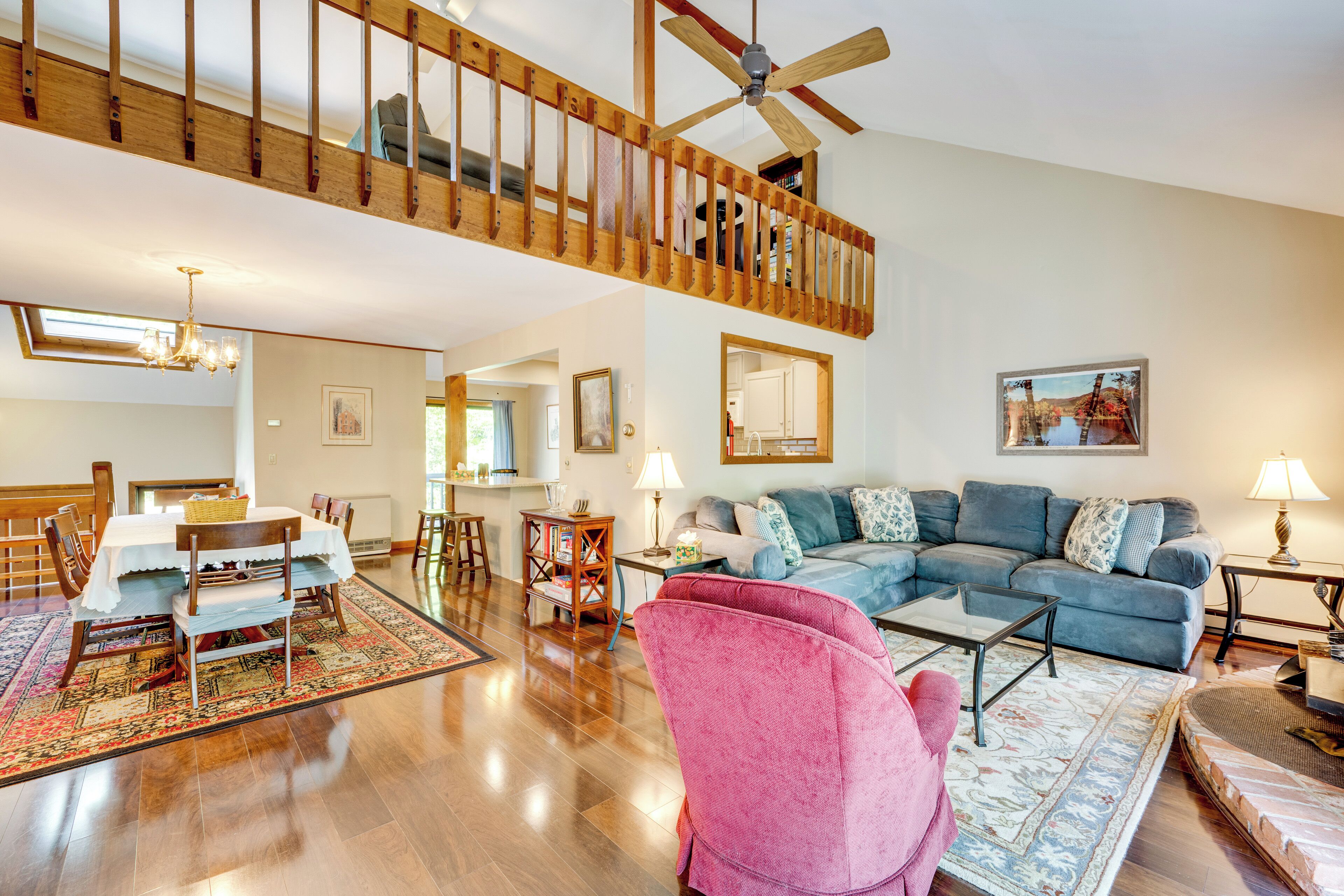 A spacious living room with a high ceiling, wooden staircase, and a dining area with a table set for four.