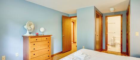 Un dormitorio con un aparador de madera, una cama con ropa blanca y un baño visible a través de una puerta abierta.