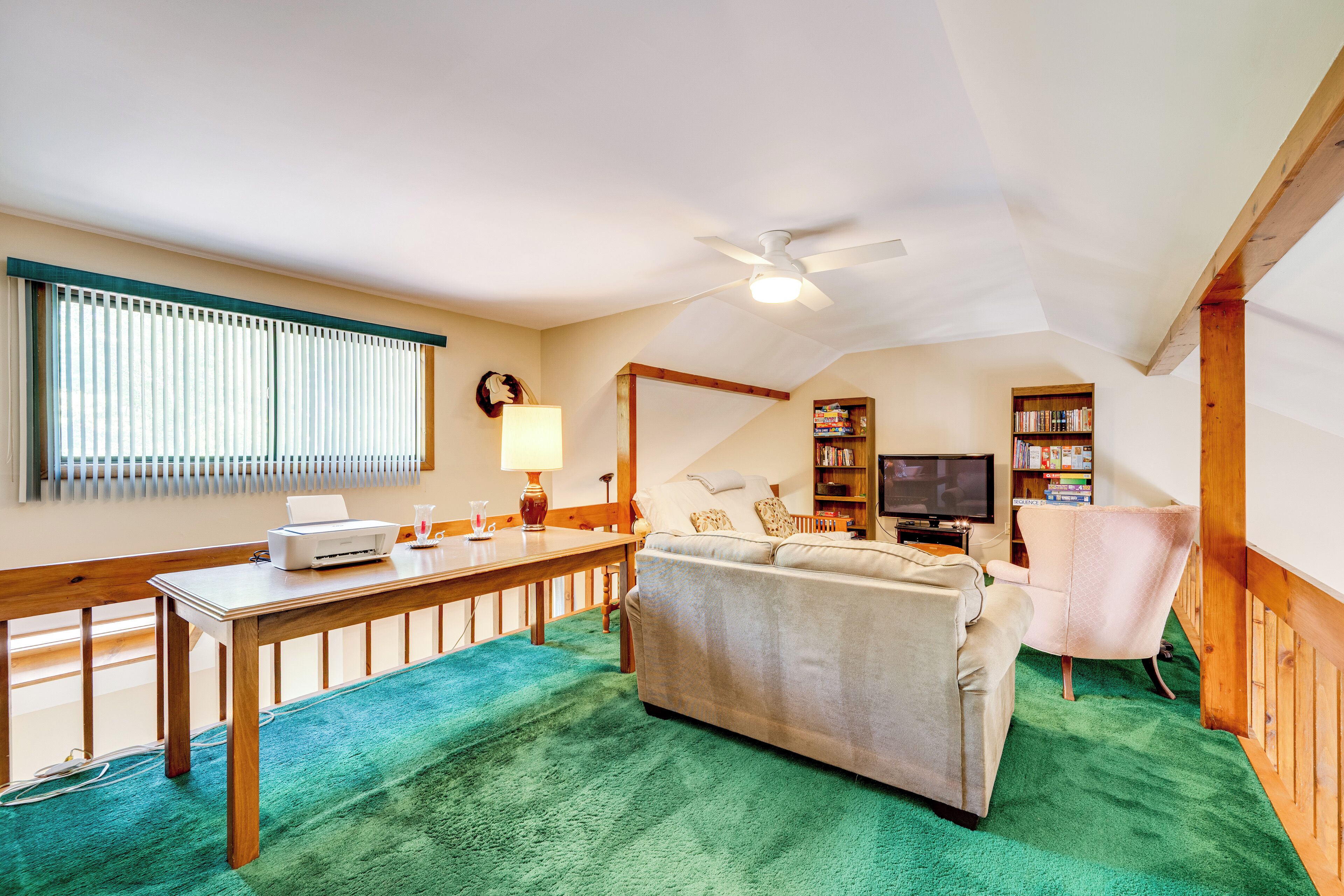 Una sala de estar acogedora con alfombra verde, un sofá, una mesa de madera, un televisor y una estantería.