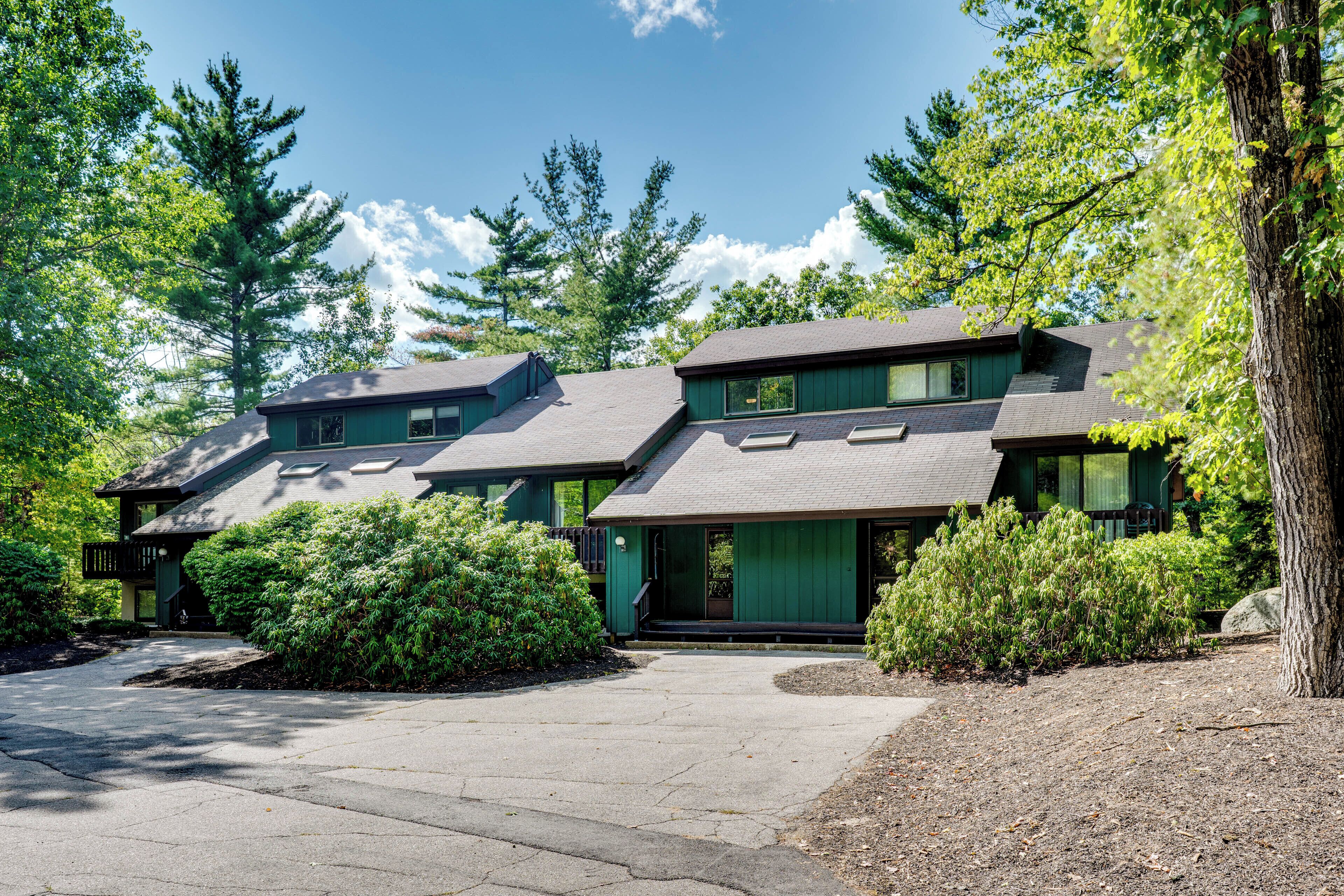 A two-story house with a green exterior, a covered front porch, and a driveway leading to the entrance.