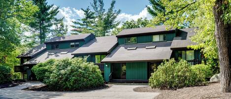 A two-story house with a green exterior, a covered front porch, and a driveway leading to the entrance.