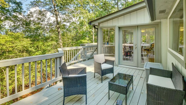 A covered outdoor deck with wicker furniture and a view of the surrounding forest.