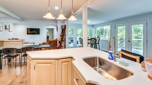 A modern kitchen with a large island, stainless steel sink, and pendant lighting.