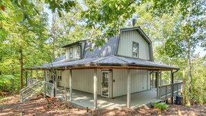 A two-story cabin with a porch and a staircase, surrounded by trees.