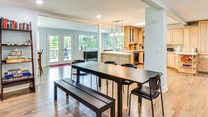 A spacious kitchen with wooden cabinets, a dining table with chairs, and a bookshelf with books and board games.