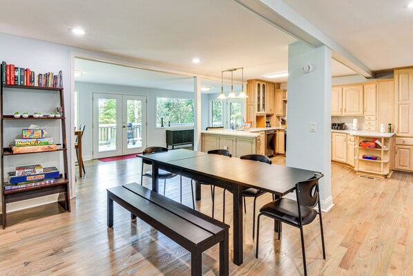 A spacious kitchen with wooden cabinets, a dining table with chairs, and a bookshelf with books and board games. - Woodsy Retreat w/ Deck & Views in Dahlonega! (Dahlonega)
