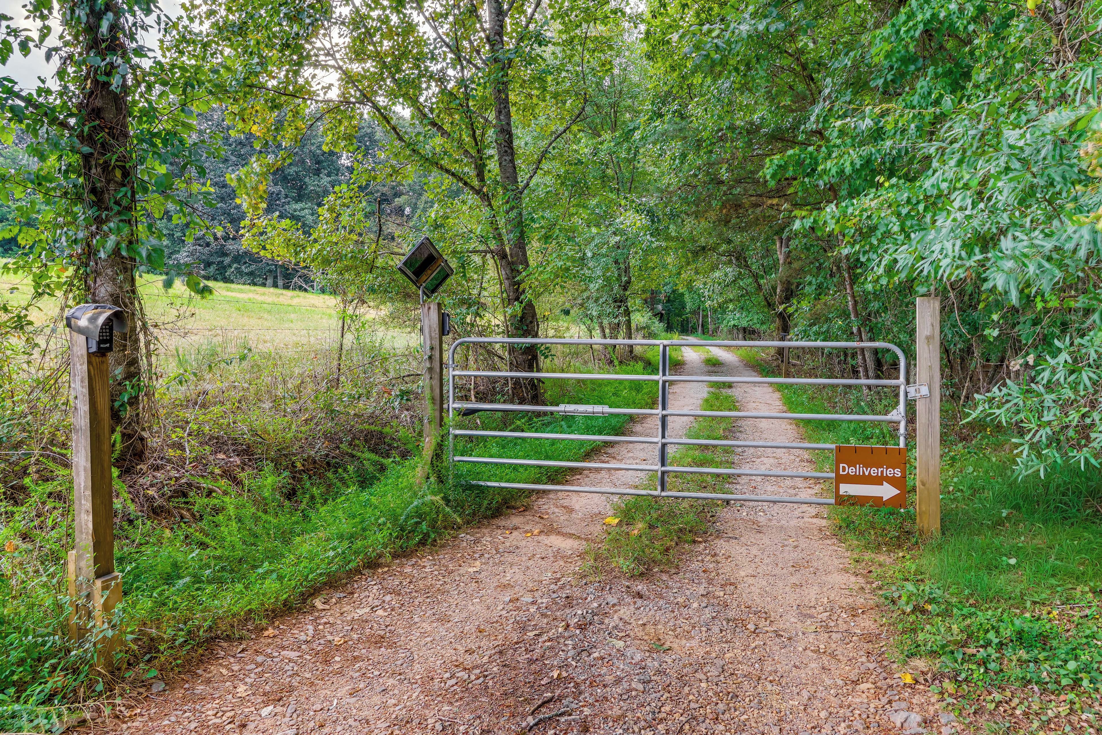 Un camino delimitado por una cerca que conduce a una zona boscosa, con un letrero que indica 'Deliveries'.