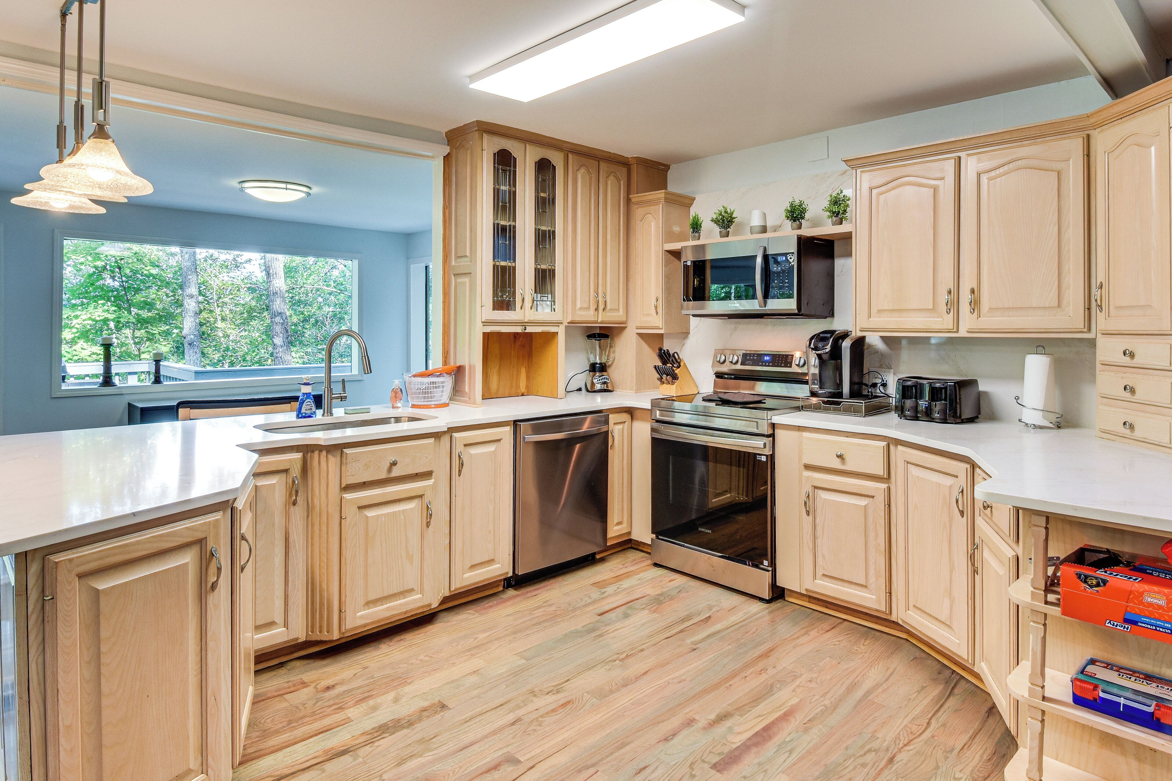 Een moderne keuken met houten kastjes, roestvrijstalen apparatuur en een groot raam met uitzicht op de omgeving.