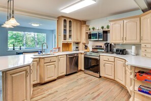 A modern kitchen with wooden cabinets, stainless steel appliances, and a large window providing a view of the outdoors. - Woodsy Retreat w/ Deck & Views in Dahlonega! (Dahlonega)