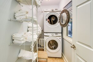 A laundry room with a front-loading washing machine and dryer, shelves with folded towels, and a small step leading to a lower shelf. - Woodsy Retreat w/ Deck & Views in Dahlonega! (Dahlonega)